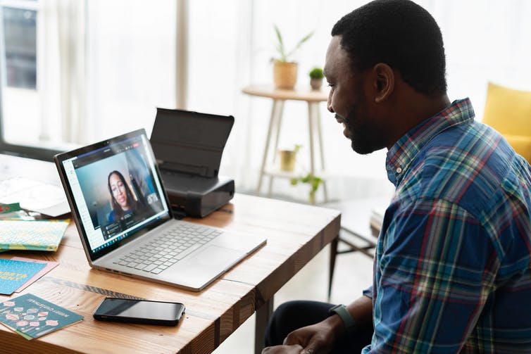 A man smiles as he talks to a woman seen on his laptop screen.