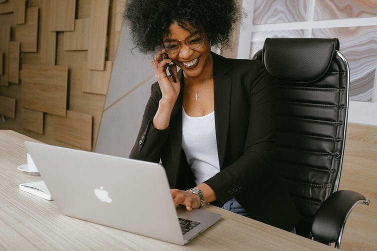 A young woman sits on the phone in front of an open laptop laughing.