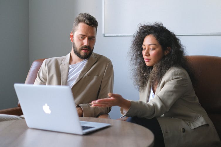 A bearded man sits next to a woman as they look at a laptop