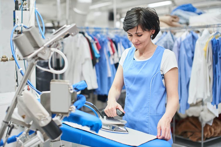 A woman in a blue apron ironing in an industrial laundry