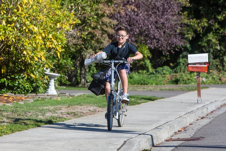 A child riding a bicycle and holding a newspaper