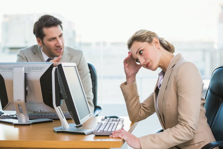 Man walking to women with head in hand, both in front of computers.