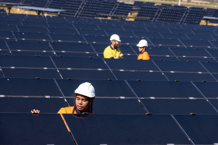 Three people are working with solar panels.