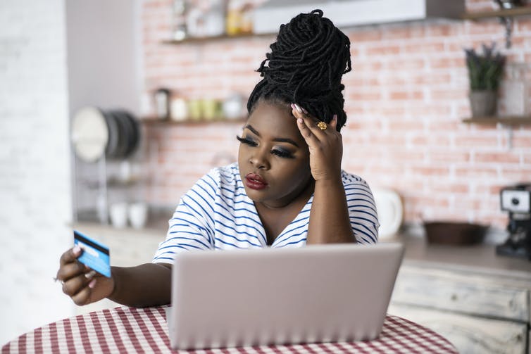 A woman stares at a credit card while her laptop is open.