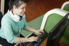 A young blind woman uses a computer with refreshable braille technology in an office setting.