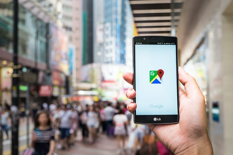 A hand holding up a mobile phone with the Google maps logo in a busy pedestrian area