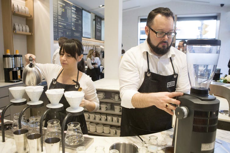 Two baristas in aprons making drinks at a café