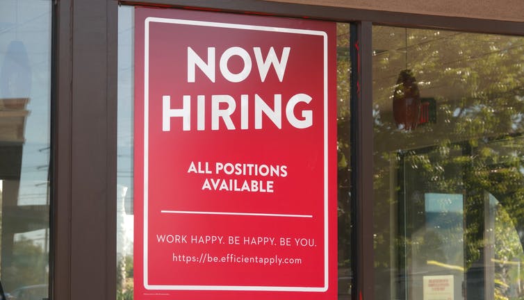 A 'Now Hiring' sign hanging in the window of a building