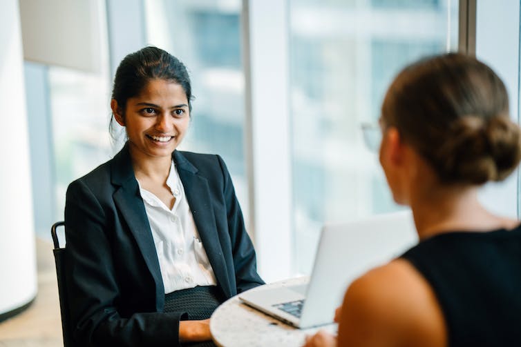 Two young women in professional clothing sit across from each other in conversation