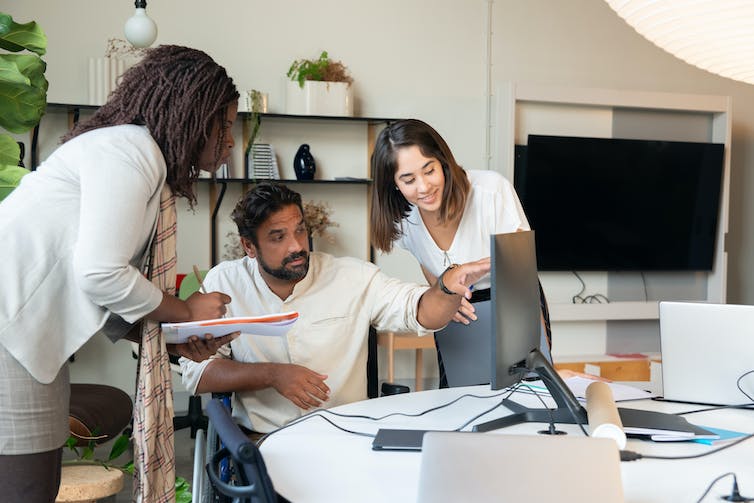 Three people having a discussion while gathered around a laptop