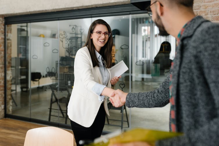 A woman shaking a young man's hand over a table