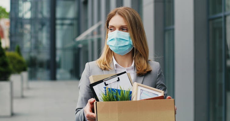 A business woman stands outside an office building holding a carboard box full of belongings