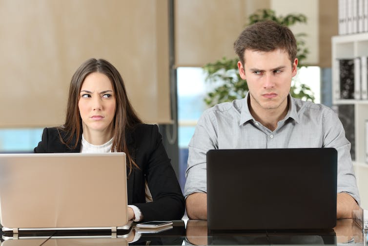 A man and woman sit at a table giving each other sideward looks.