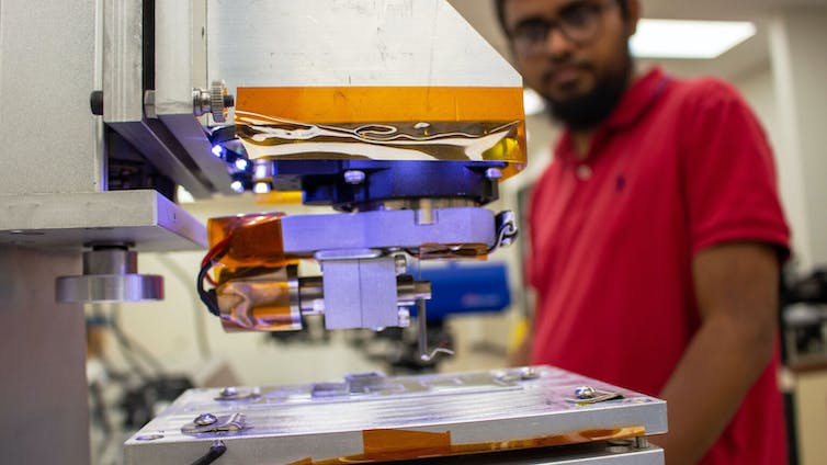 A man stands beside a 3-D printer in a university lab.