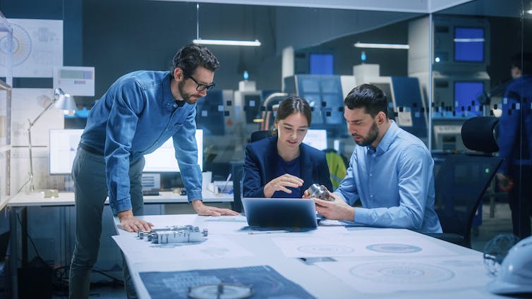 Three people huddle around laptop screen, deep in discussion.