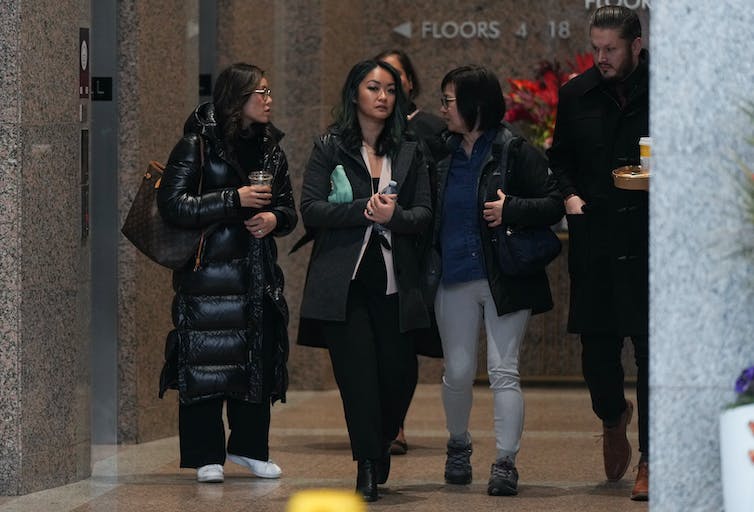 Three Asian women dressed in black winter coats leave a courthouse.