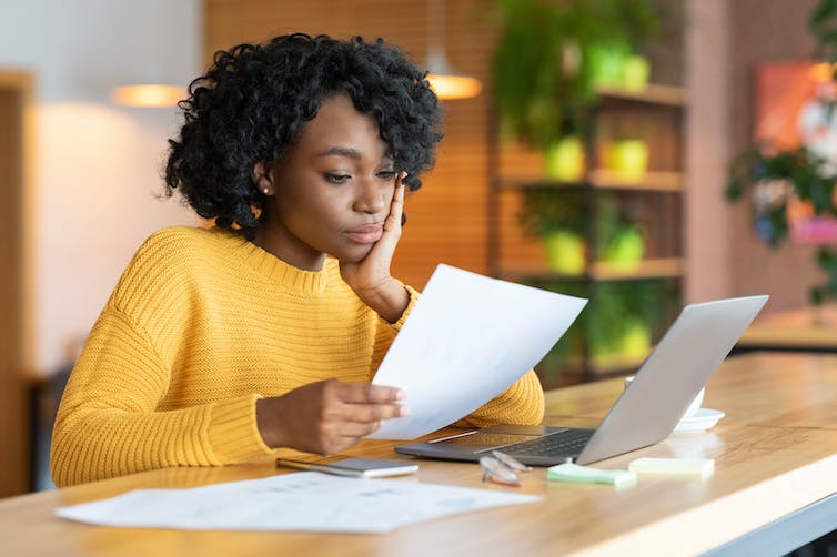 A young woman sitting at a desk reading a sheaf of paper