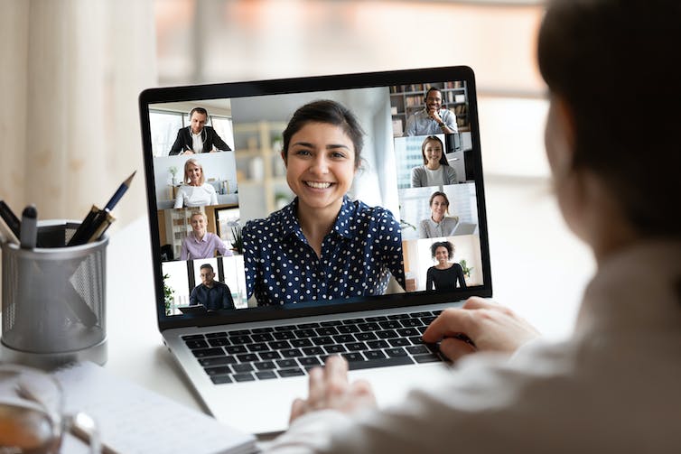 An open laptop with a virtual meeting taking place on it seen from over someone's shoulder.