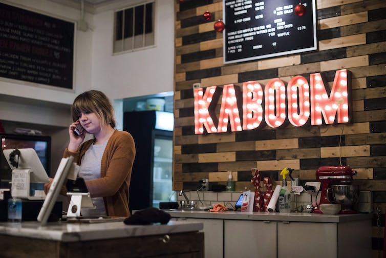 A young woman speaks on the phone as she works behind a cash register in a fast-food restaurant