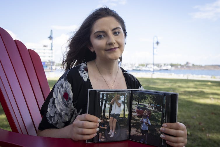 A young woman holds open a photo album to display photos of a man on a rope swing and the same man with a little girl sitting on his shoulders