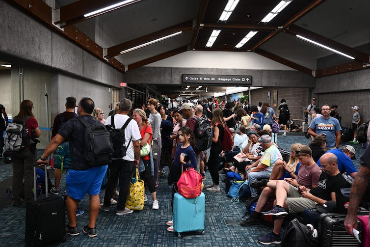 People standing, sitting and lying down around an airport departure gate.