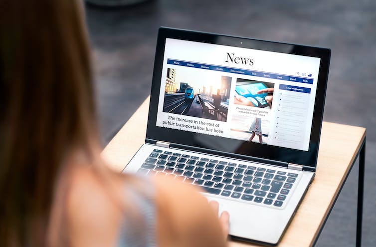 An laptop open to a news article is seen over the shoulder of a young woman