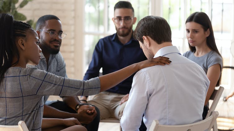 A group of people sit in a circle consoling a man.