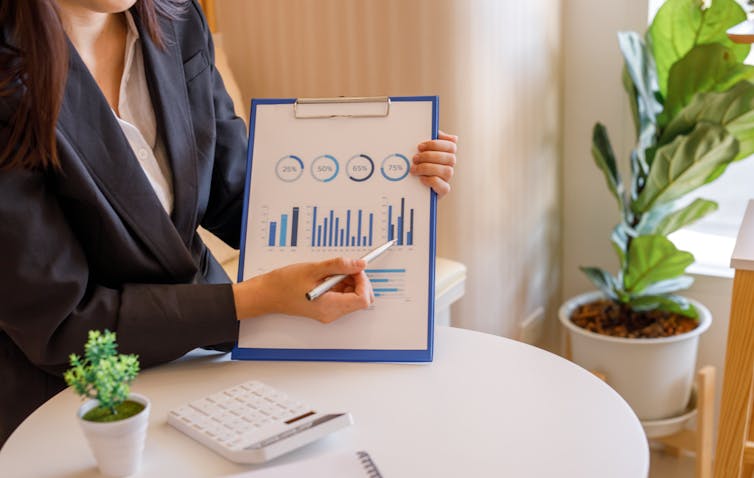 A person, seen from the neck down, pointing to a graph on a clipboard with a pen