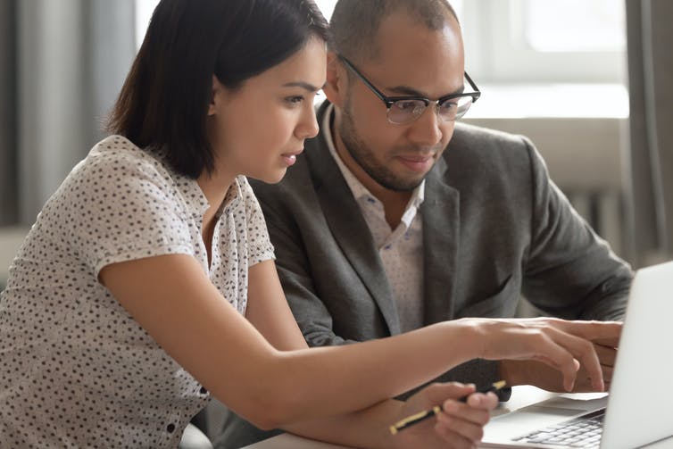 A man and a woman looking at a computer screen together. The woman is pointing at the screen.