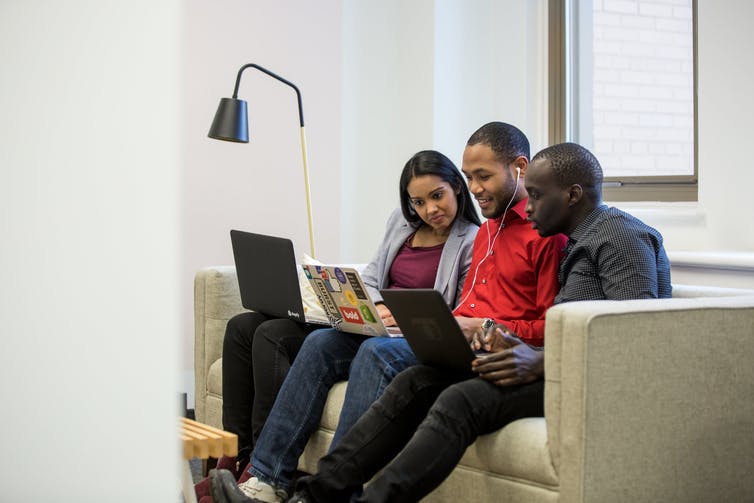 Three racialized young people laugh while looking at their laptops.