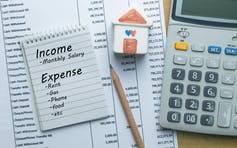 A list of household expenses and income is placed on top of a bill with a calculator beside it